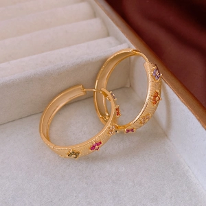 Close-up of gold-plated hoop earrings with colorful zircon floral accents and texture