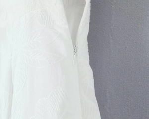 Détail du tissu brodé blanc avec motifs floraux et fermeture éclair latérale