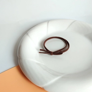 Detail of high-elastic coffee brown hair tie with knot design on white ceramic plate