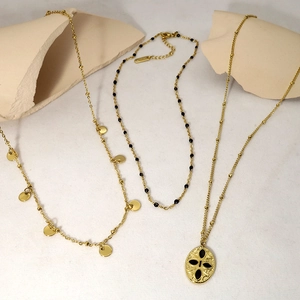 Detailed view of layered gold necklaces with oval enamel pendant and beaded chain texture