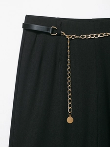 Dettaglio dei pantaloni neri con cintura a catena dorata e inserti in pelle in vita