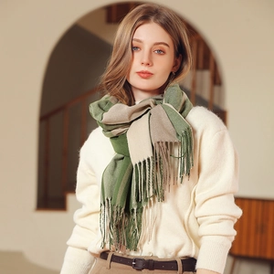 Thick green and beige plaid scarf with tassels on model in a cozy interior setting