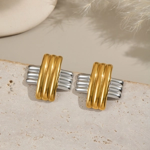 Minimalist gold and silver striped cross earrings on a beige stone with natural decor