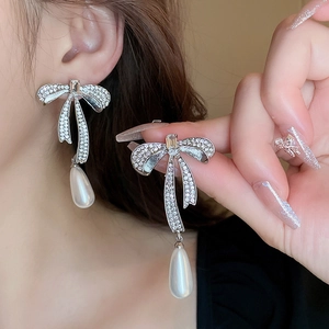 Elegant silver bow earrings with sparkling rhinestones and drop pearls worn by a model