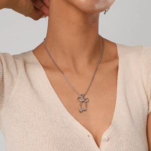 Silver bow necklace with heart pendants on a metal snake chain worn by a model