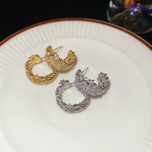 Detailed view of gold and silver C-shaped earrings with sparkling cubic zirconia on ceramic plate