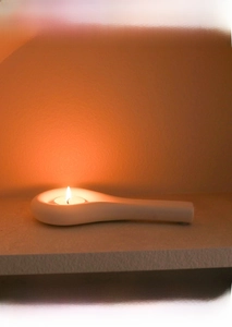 Detail of a minimalist white ceramic tea light holder with candle on a shelf