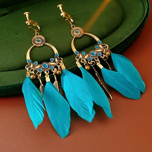 Détail de boucles d'oreilles bohèmes dorées avec plumes bleues sur boîte velours
