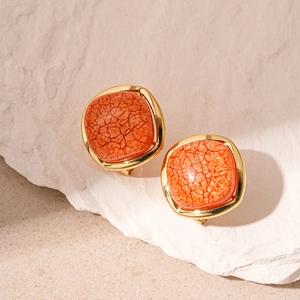 Close-up of square resin earrings with orange texture and gold plating on stone base