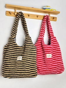 Striped sherpa fleece tote bags in pink and khaki hanging on a wooden wall rack