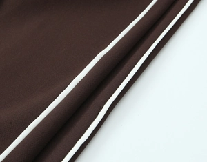 Close-up of the contrast side stripe stitching on dark brown blended fabric trousers