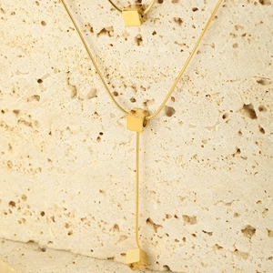 Macro shot of gold cube pendant on snake chain over natural yellow stone background