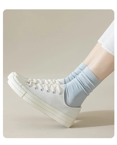 Close-up detail of women's light blue mid-calf cotton socks worn with white canvas shoes.