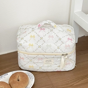 Détail d'une trousse à maquillage matelassée fleurie avec nœuds et fermetures à ruban