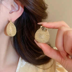 Detail of vintage oval gold earrings with intricate woven texture on a model's ear
