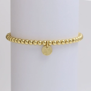 Detail of a golden beaded stretch bracelet featuring a round letter N initial pendant