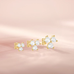 Detailed view of three sizes of gold heart-shaped clover stud earrings with clear zircons