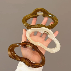 Detail of large acrylic wave-shaped hair claws in dark green, cream and amber colors