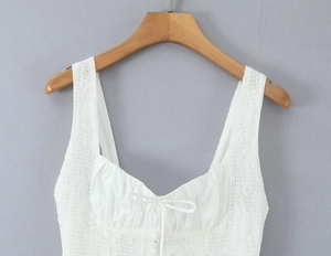 Detail of white lace camisole with square neck, pleats, bow and buttons on a hanger