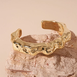 Macro view of gold minimalist irregular lava texture open cuff bracelet on stone