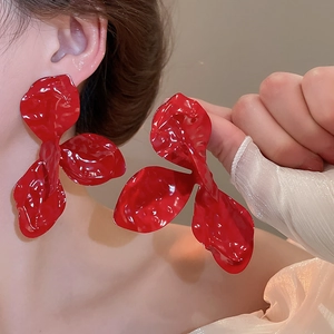Close-up of oversized red pleated flower earrings with textured matte finish