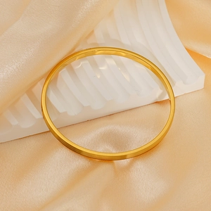 Detailed close-up of polished gold-plated stainless steel bangle on elegant silk