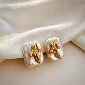 Macro shot of gold floral metalwork on white baroque pearl earrings on beige silk fabric