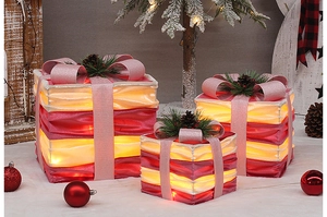 Close-up of three pink and red Christmas gift boxes with bows and warm LED lights