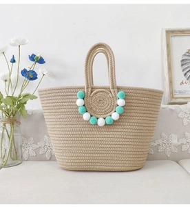 Detail of handmade beige straw tote bag featuring decorative white and teal pompoms