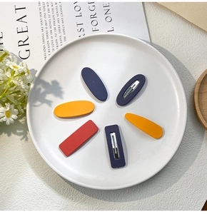 Flat lay of colorful matte hair clips in blue, orange, and yellow on a white ceramic plate