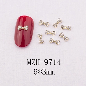 Détail macro de charmes de nœud doré 6x3mm avec zircons blancs sur ongle rouge