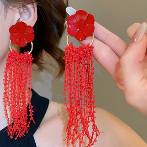 Macro shot of long red beaded tassels and painted flower earrings worn by a model