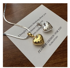 Dettaglio ravvicinato di ciondoli a cuore testurizzati in oro e argento con catena snake