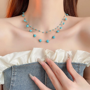 Close-up of double-layer gold necklace with turquoise blue heart beads on a model's neck
