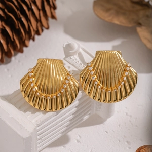 Gold shell stud earrings with zircons on white column stand in natural autumn setting