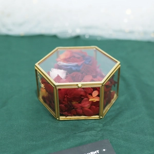 Detail of hexagonal glass ring box with gold metal frame and dried red flower petals