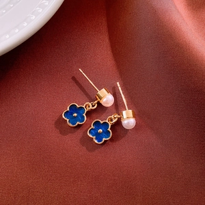 Detail of gold floral earrings with deep blue petals and pearls on a textured background