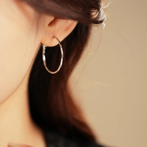 Close-up of polished silver hoop earring with wavy hammered texture on female model