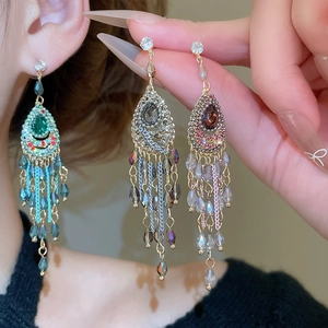 Detailed view of long rhinestone tassel earrings in emerald and champagne crystal tones