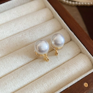 Macro shot of elegant gold pearl ear clips resting in a luxury fabric jewelry box