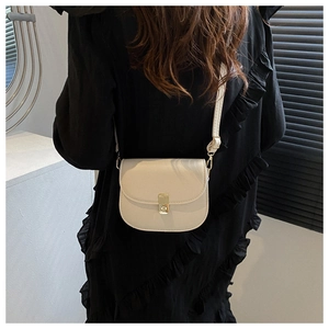 Detail of cream saddle bag with gold buckle worn against a black dress background