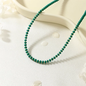 Detail of emerald green beaded necklace with gold spacers on white textured fabric