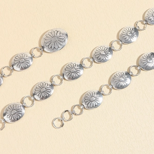 Detail of vintage metal waist chain featuring engraved daisy patterns on silver oval links