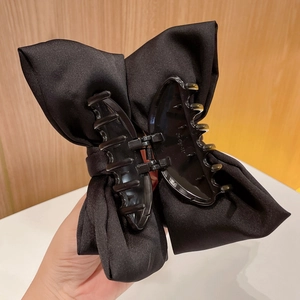 Close-up of a large black satin bow hair claw clip held against a soft background