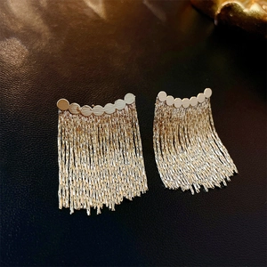Macro shot of elegant golden metallic tassel earrings with fringe on black leather texture