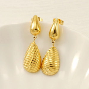Elegant gold teardrop earrings with textured grooves resting on a ceramic dish