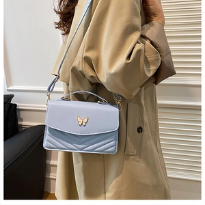 Detail of blue quilted crossbody bag with golden butterfly clasp on khaki trench coat