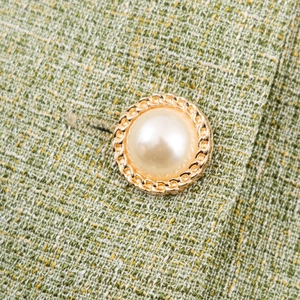Detail of green tweed jacket featuring a gold braided button with a pearl dome center