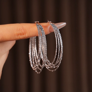Detail of silver multi-layered hoop earrings with diamond-cut texture held by hand