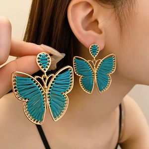Detail of vintage bohemian butterfly earrings with gold frame and peacock blue woven thread